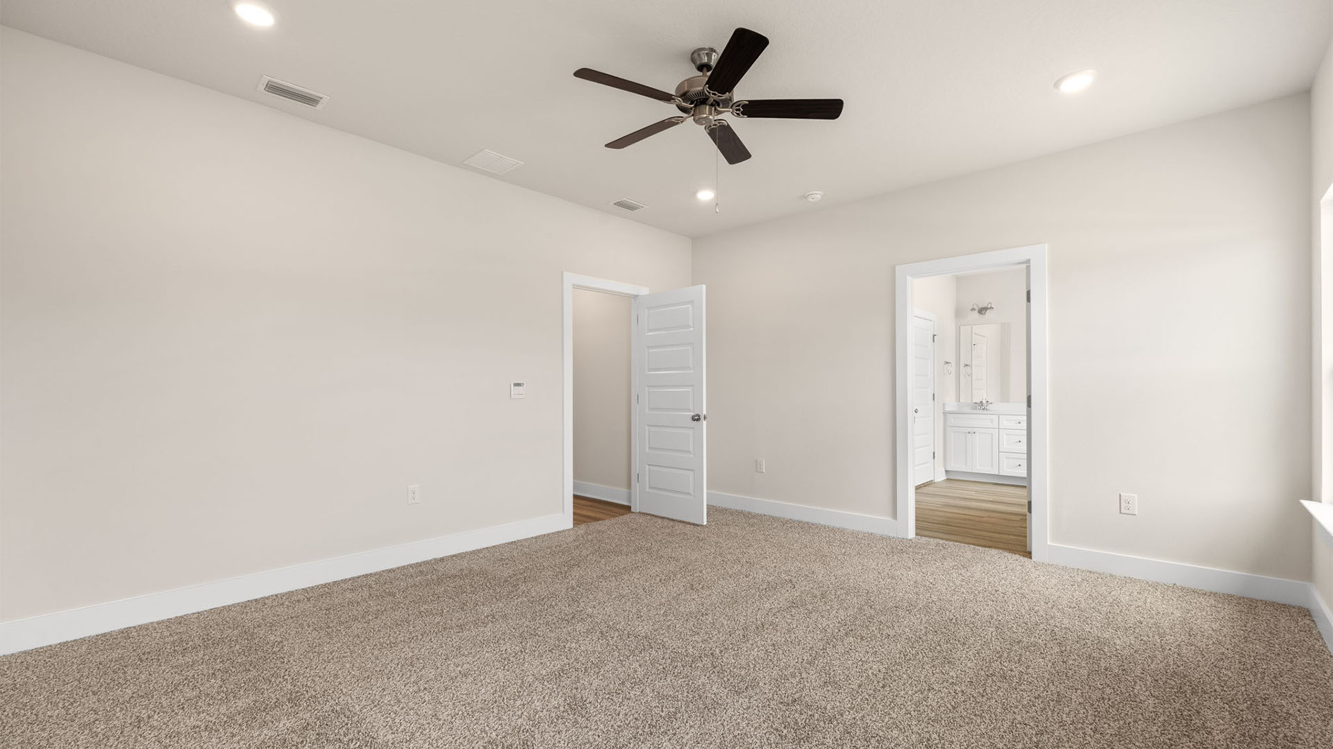 Primary bedroom with carpet flooring and ceiling fan and bathroom entrance.