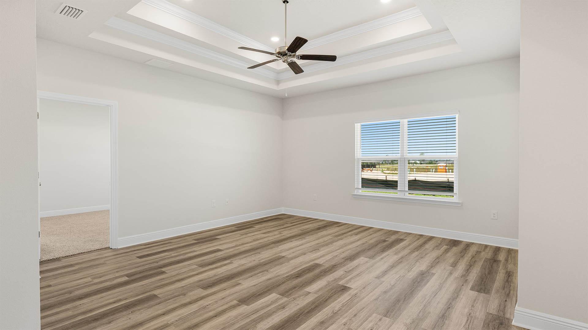 Open living room with tray ceilings and ceiling fan and EVP flooring and window and primary bedroom entrance.