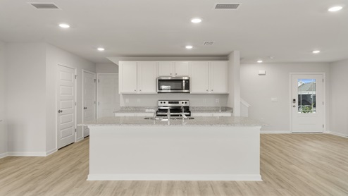 Kitchen with island and granite countertops and white cabinetry and stainless-steel appliances.