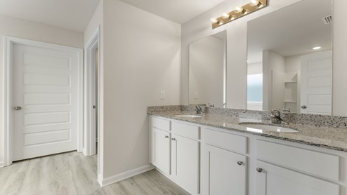 Primary bathroom with double vanity granite countertops and closet entrance.