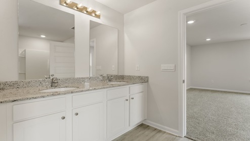 Primary bathroom with double vanity granite countertops and bedroom entrance.