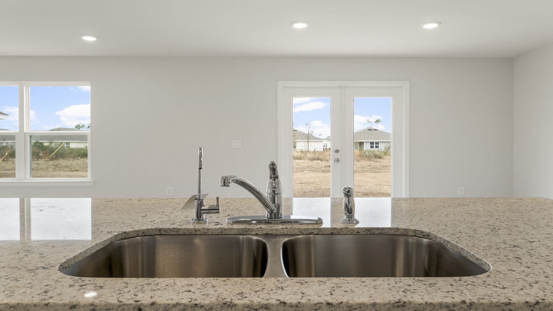Kitchen island with granite countertops and undermount sink looking into dining area and back door.