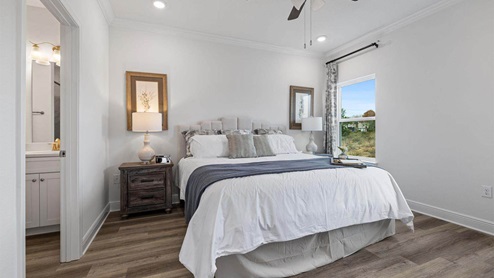 Primary bedroom with EVP flooring with ceiling fan and window and bathroom entrance.