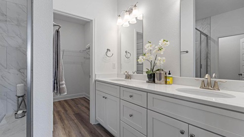 Primary bathroom with double vanity quartz countertops and white cabinets and tile shower and closet with EVP flooring.