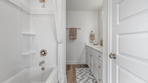 Bathroom with single vanity quartz countertops and white cabinets and shower and tub with EVP flooring.