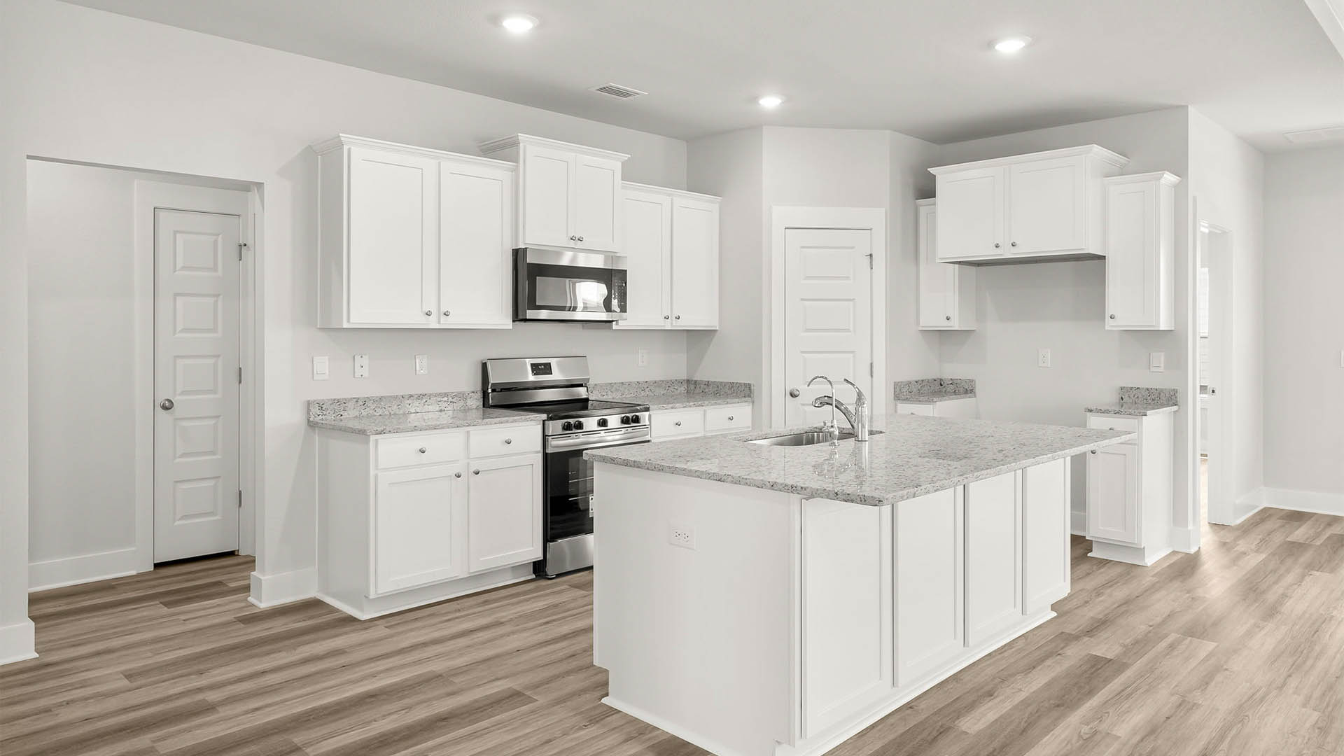 Open kitchen with island and granite countertops and white cabinets and stainless steel appliances and pantry.