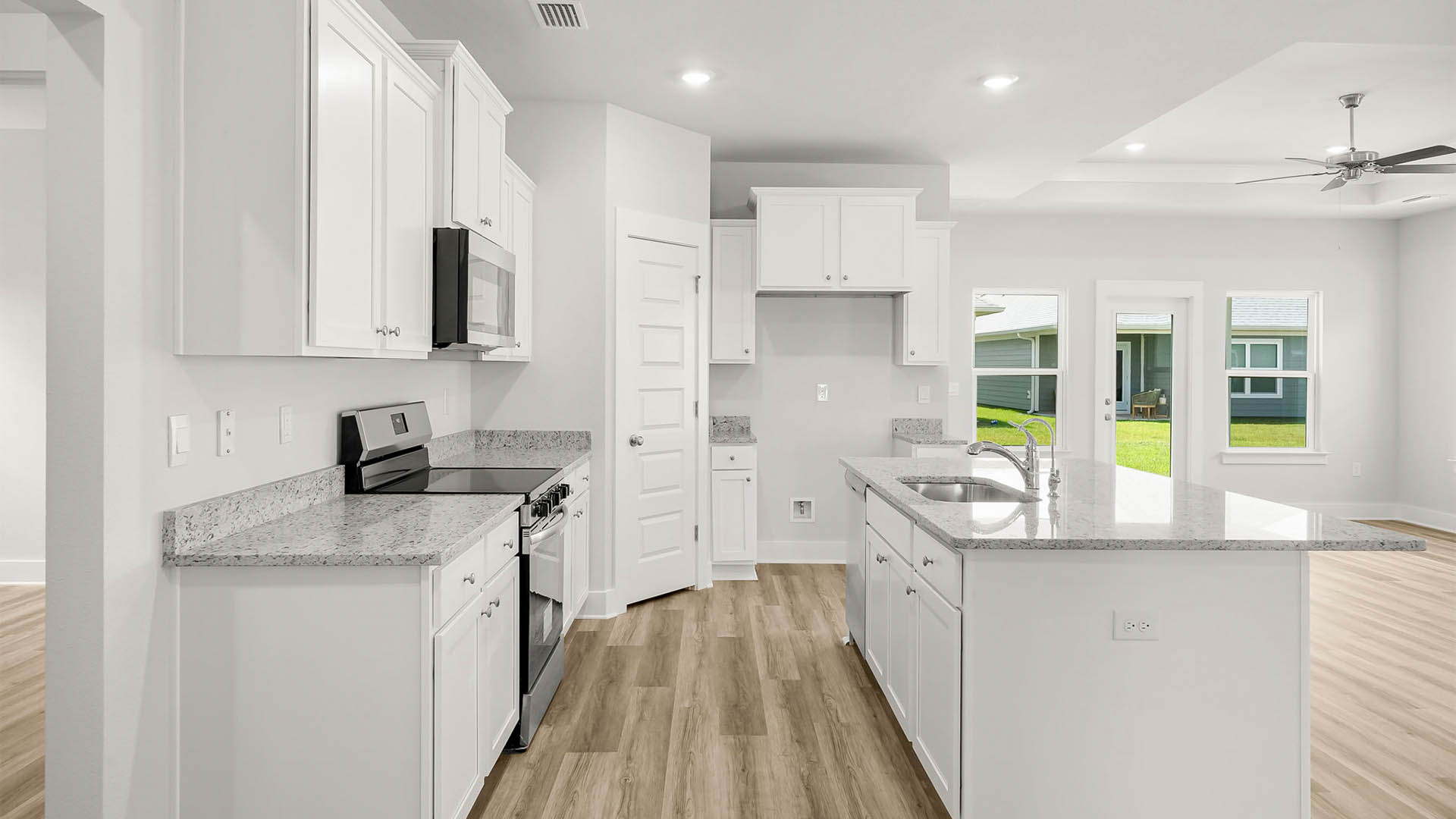 Open kitchen with island and granite countertops and white cabinets and stainless steel appliances and pantry.