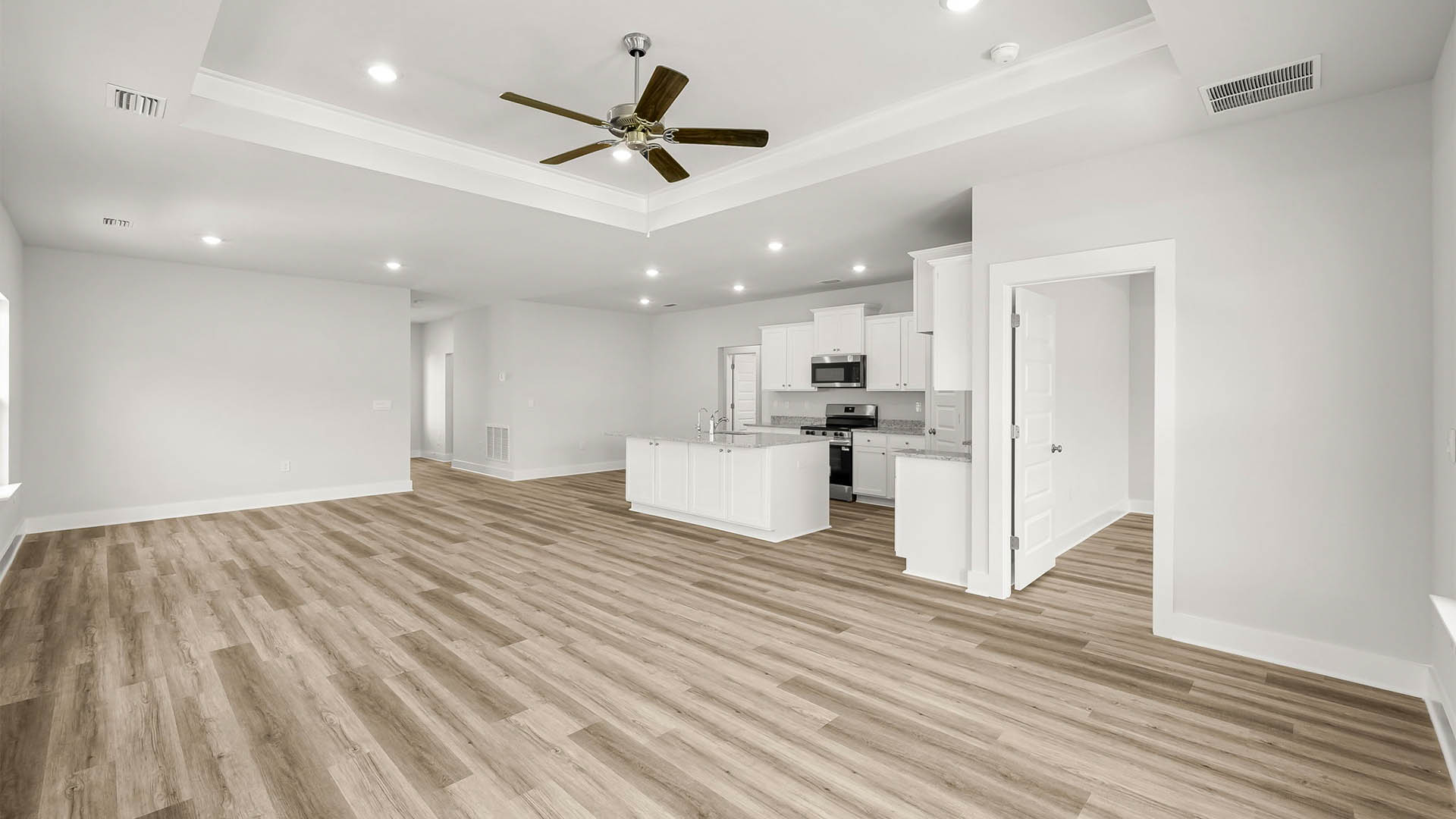 Open living room with ceiling fan and EVP flooring and kitchen next to primary bedroom.