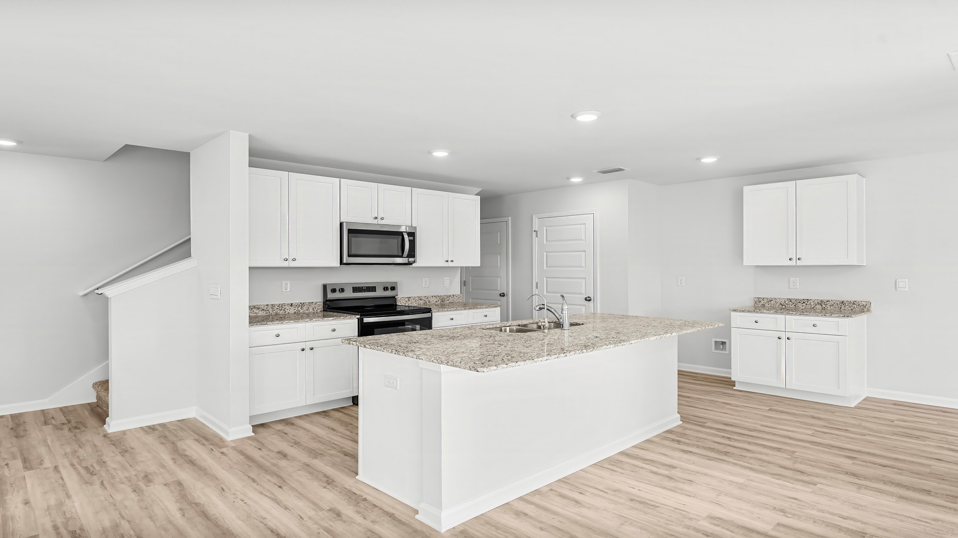 Kitchen with island and granite countertops and white cabinetry and stainless-steel appliances.