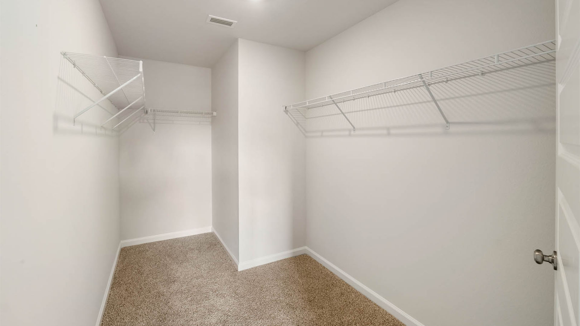 Walk in closet with ventilated shelving and carpet floor.