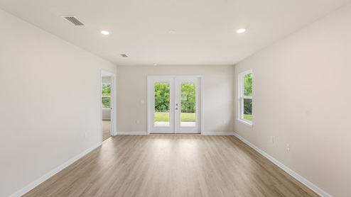 Open living room with dual back doors and primary bedroom entrance and window.