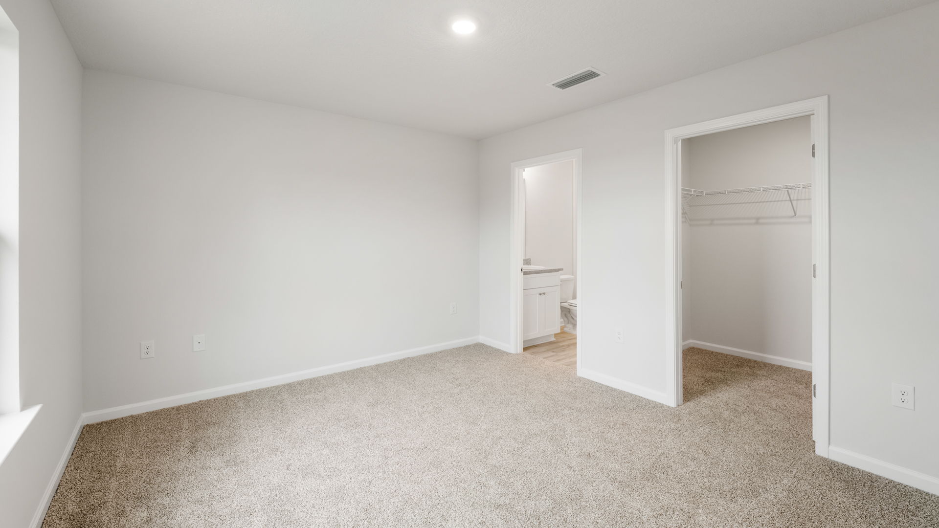 Primary bedroom with carpet floors and walk-in closet and bathroom entrance.