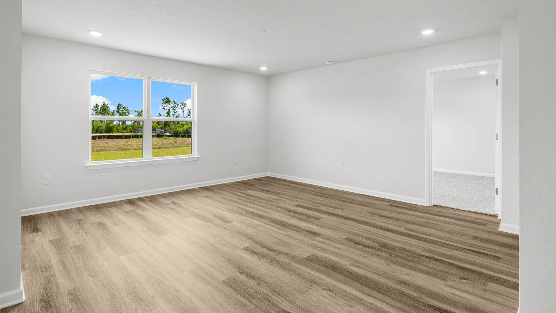 Open living room with EVP flooring and two windows next to primary bedroom entrance.