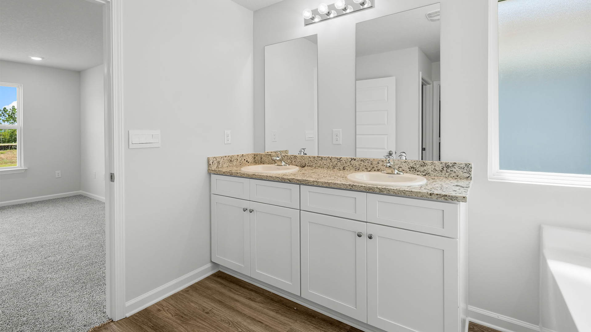 Primary bathroom with double vanity granite countertops and white cabinets.