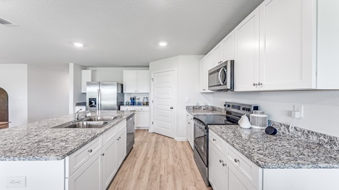 Open kitchen with island and granite countertops and stainless-steel appliances and white cabinets.
