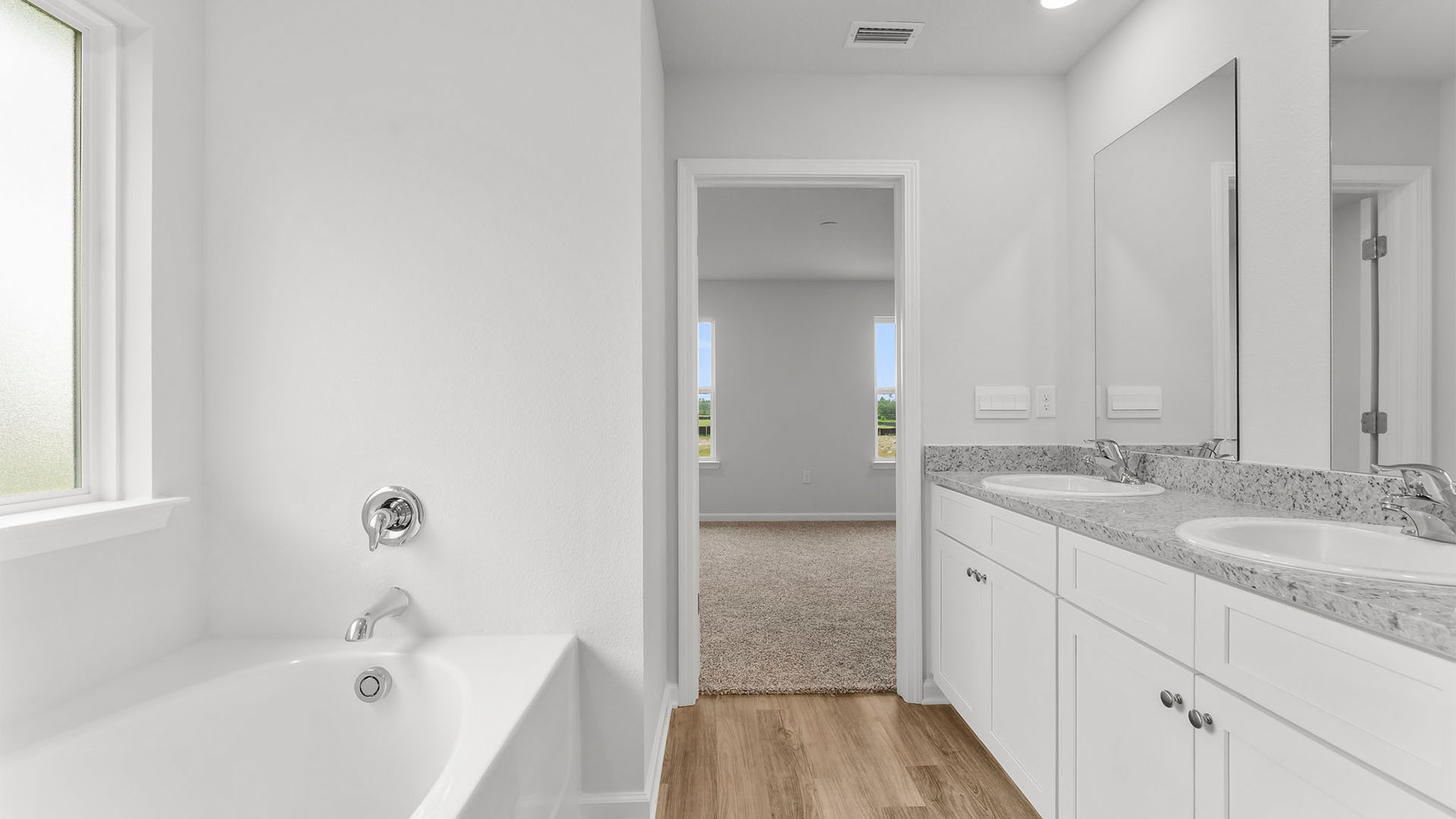 Primary bathroom with double vanity granite countertops and tub and closet.