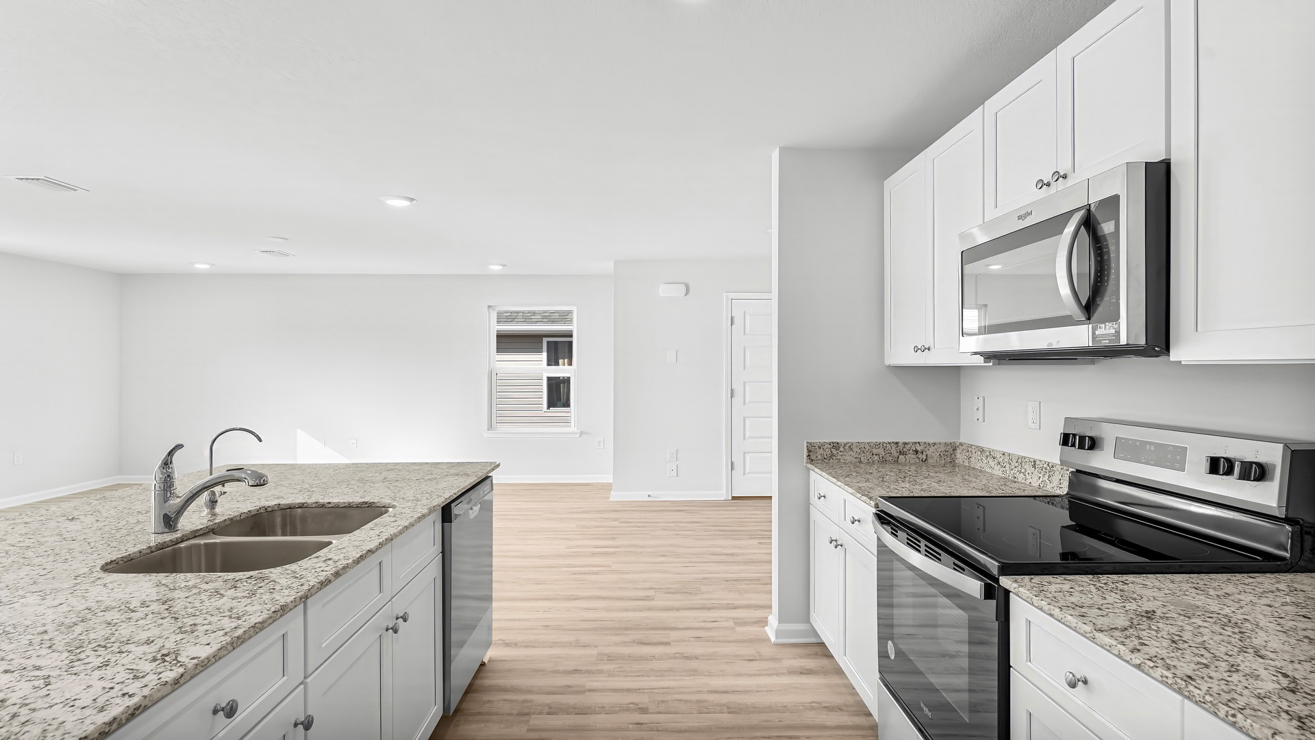 Kitchen with island and granite countertops and white cabinetry and stainless-steel appliances.