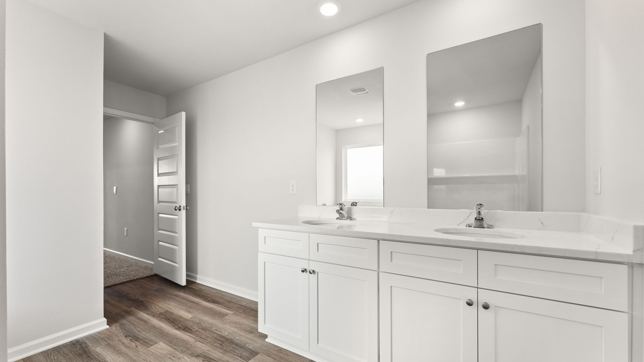 Primary bathroom with double vanity sinks and quartz countertops with white cabinets and EVP flooring.