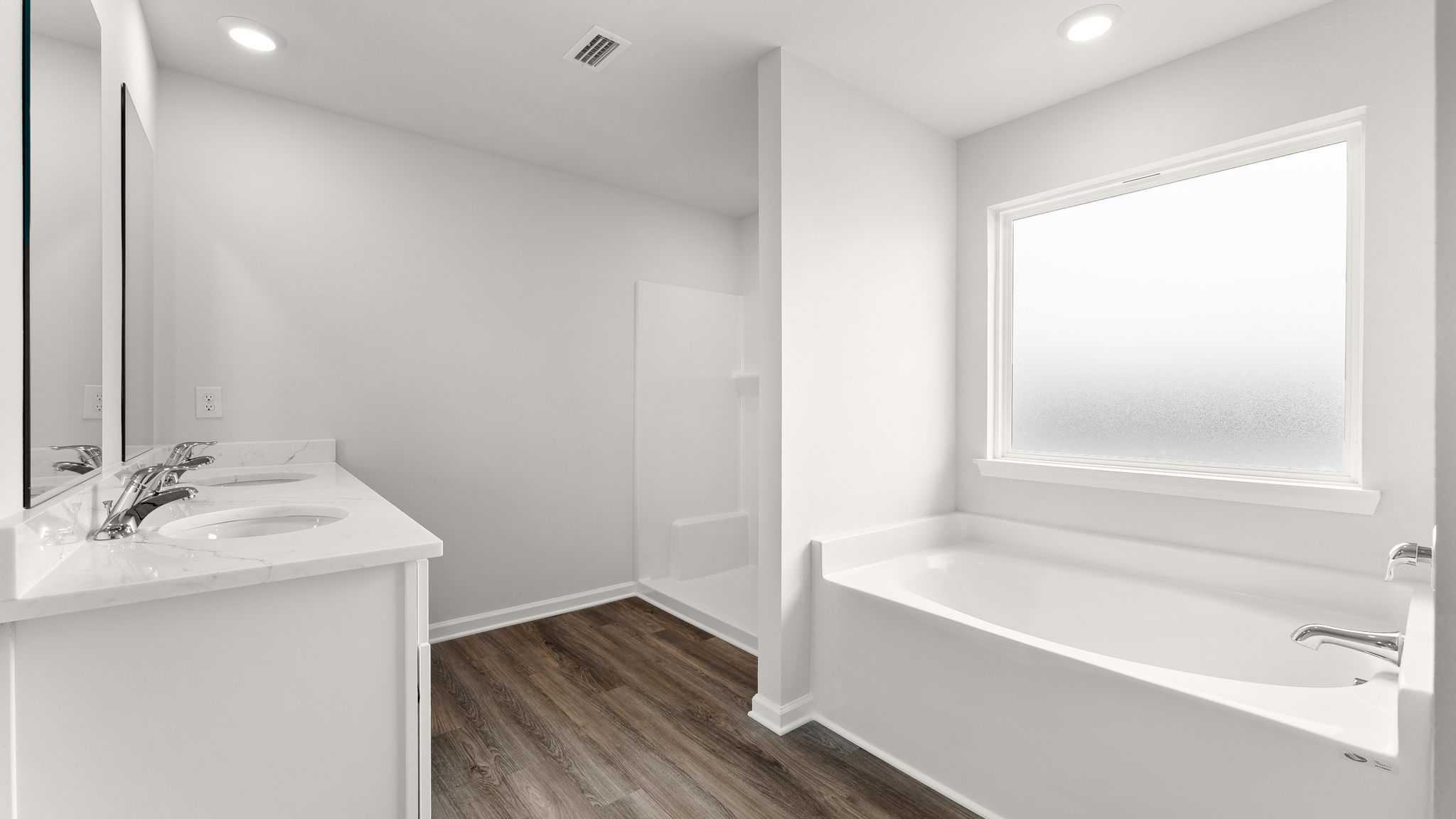 Primary bathroom with double vanity sinks and quartz countertops with white cabinets and EVP flooring and shower and tub.