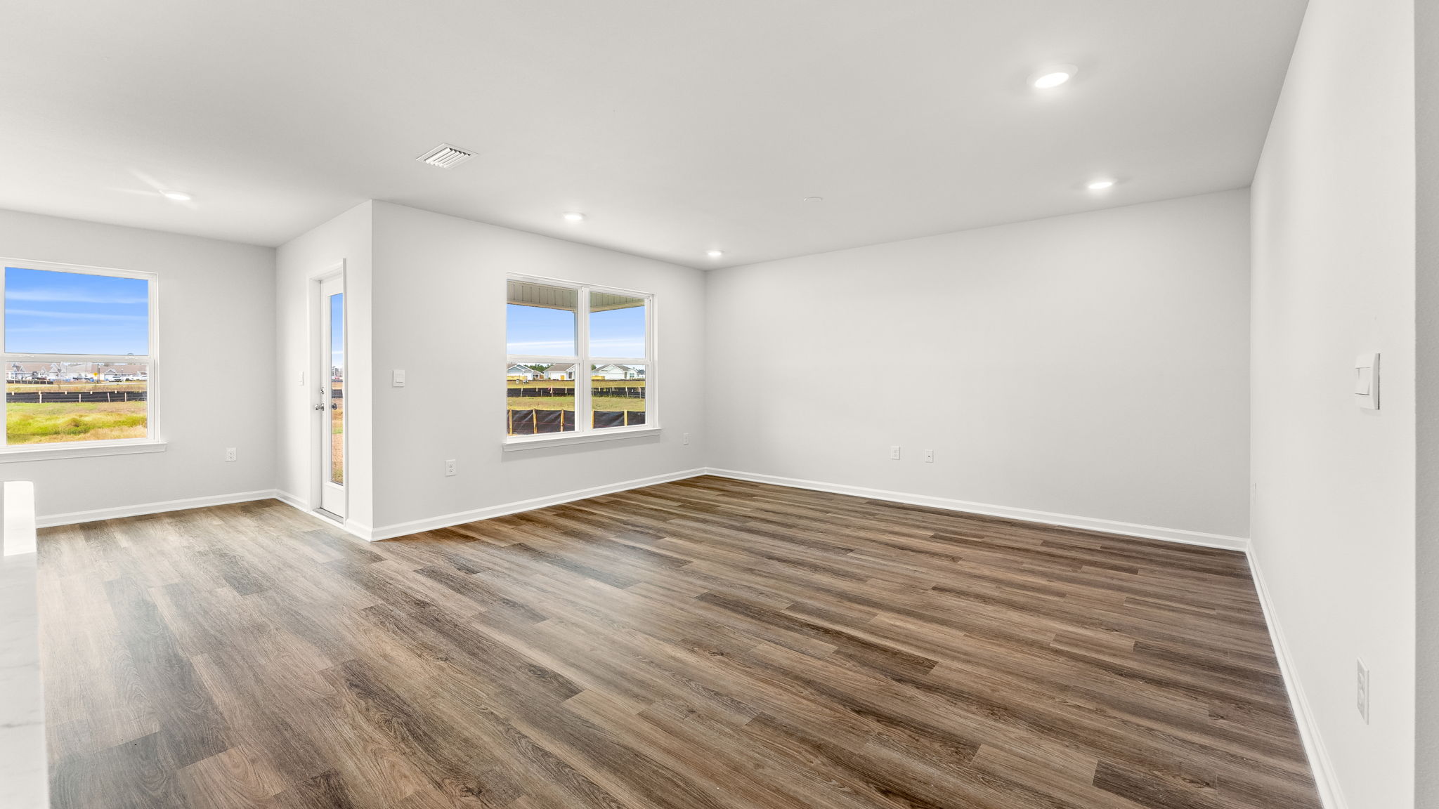 Living room with windows and EVP flooring next to kitchen and back door.