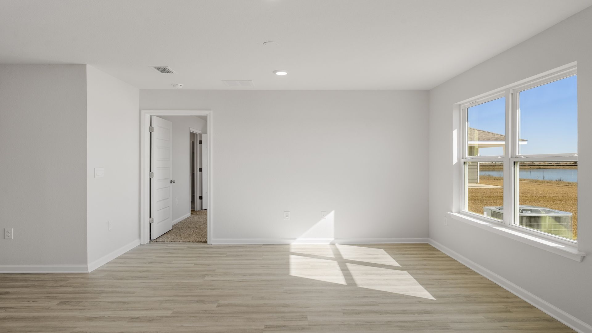 Open living room with two windows and bedroom door.