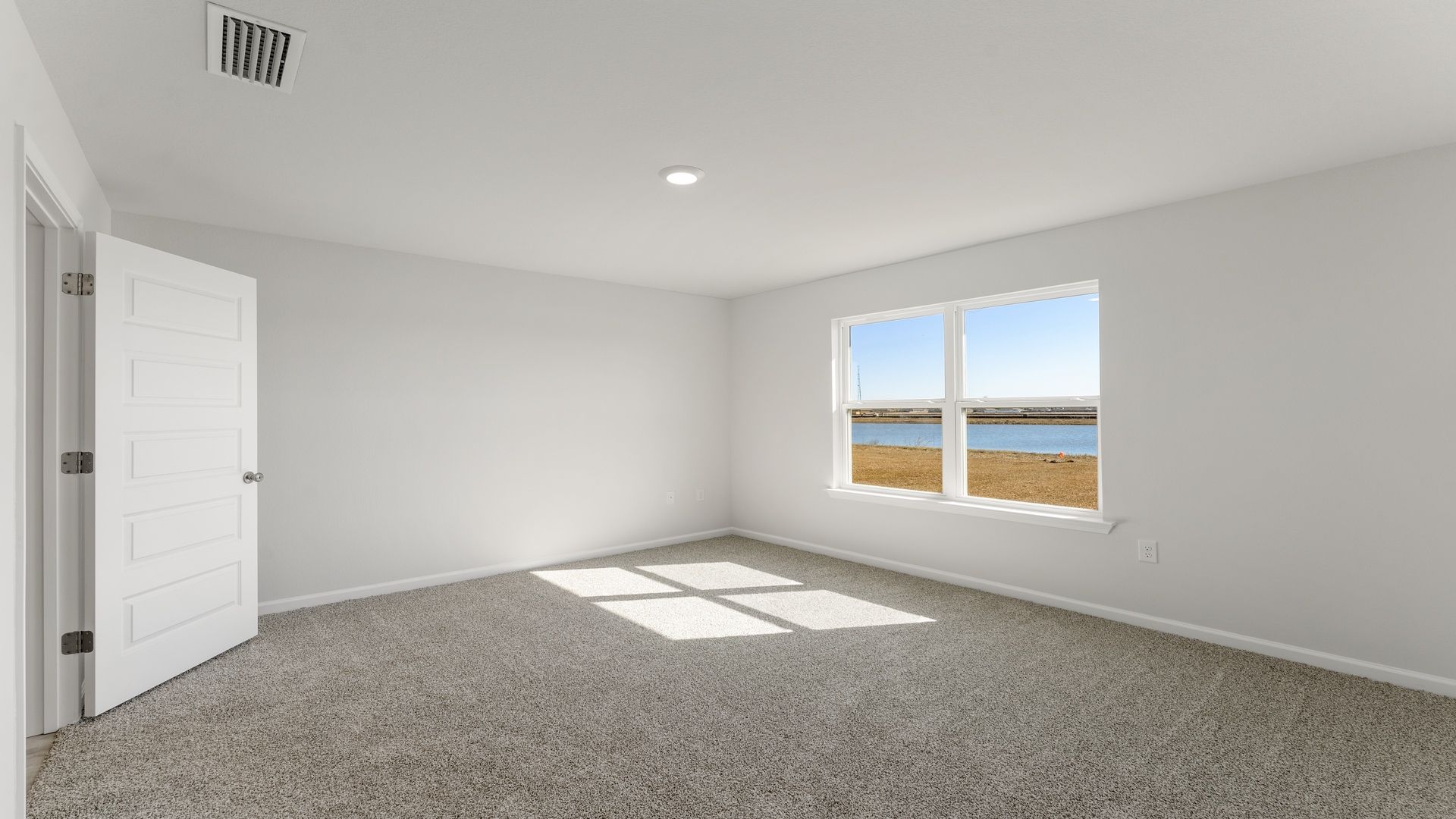 Primary bedroom with carpet floors and two windows and bathroom door.