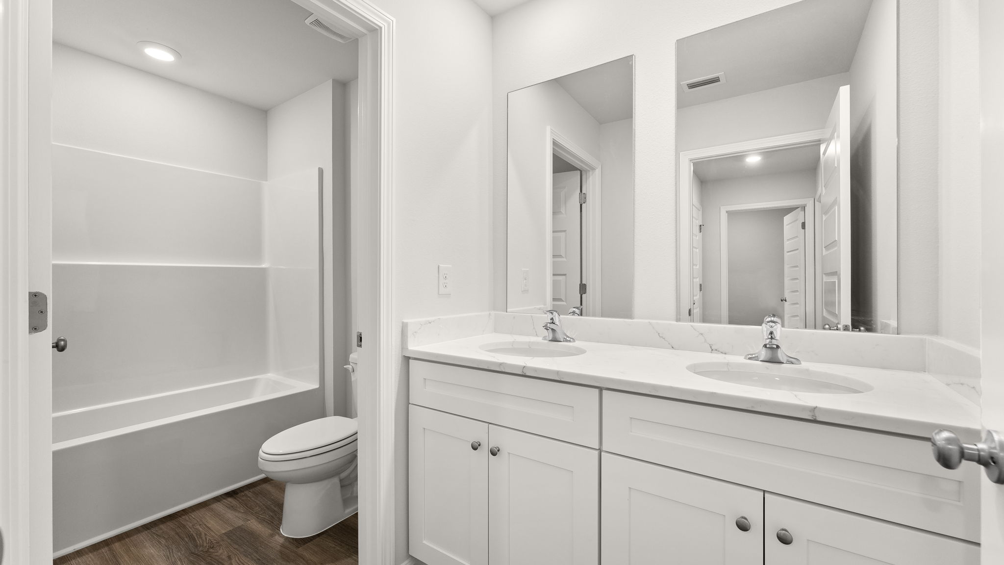 Bathroom with double vanity sink and quartz countertops with white cabinets and EVP flooring and shower and toilet.