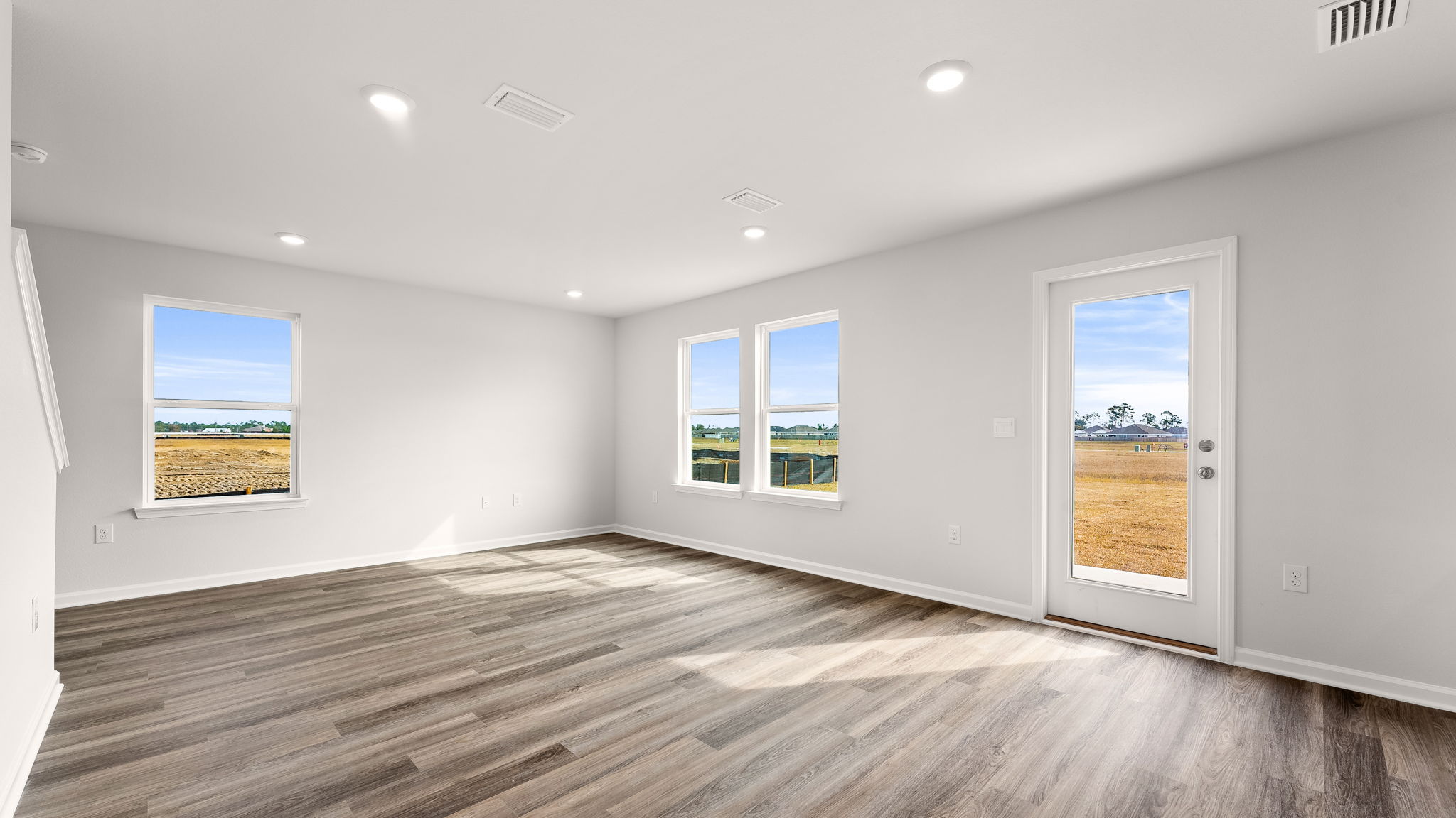 Living room with EVP flooring and windows and back door next to kitchen.