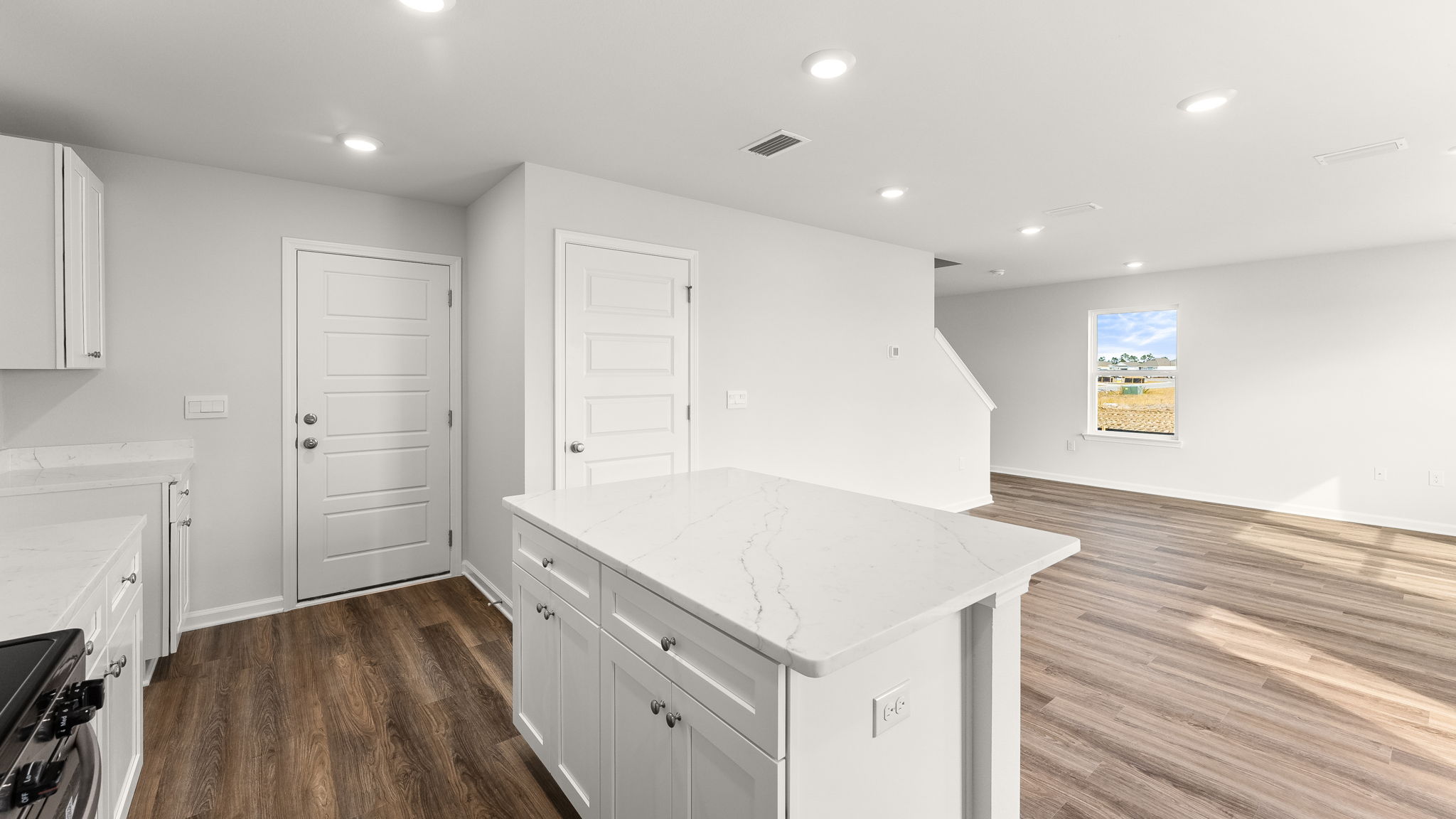 Kitchen with island and quartz countertops with white cabinets and stainless-steel appliances and pantry and garage door.
