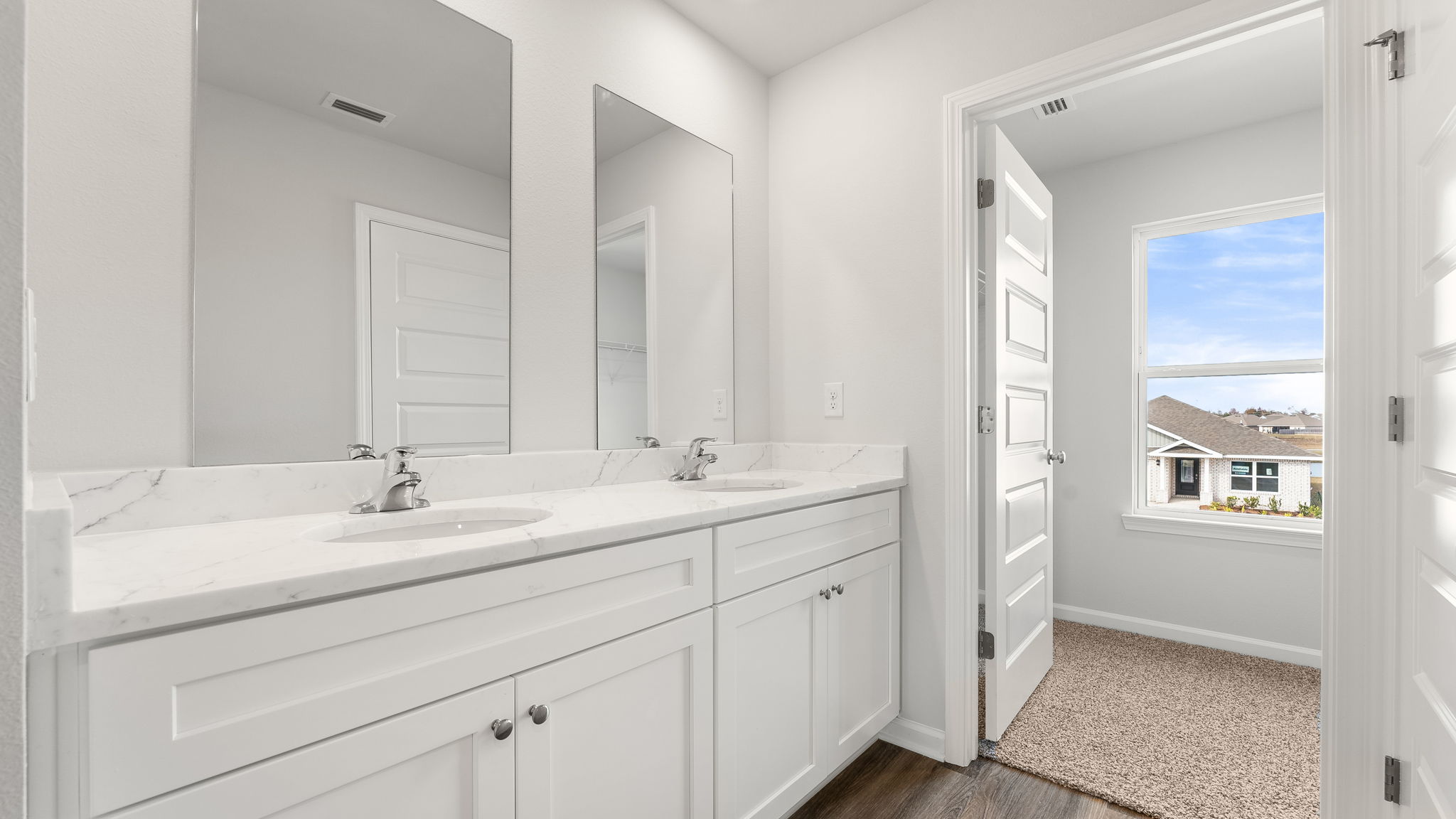 Primary bathroom with double vanity sinks and quartz countertops with white cabinets and EVP flooring.