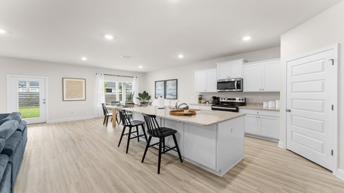 Open kitchen with island and granite countertops and white cabinets and stainless steel appliances and pantry.