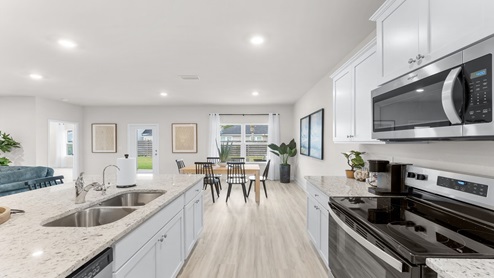 Open kitchen with island and granite countertops and white cabinets and stainless steel appliances and pantry and dining area.
