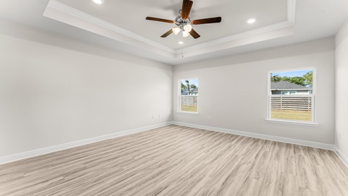 Primary bedroom with EVP flooring and ceiling fan and tray ceilings and windows.