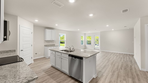 Open kitchen with island and granite countertops and white cabinets and stainless-steel appliances looking into open living room with EVP flooring.