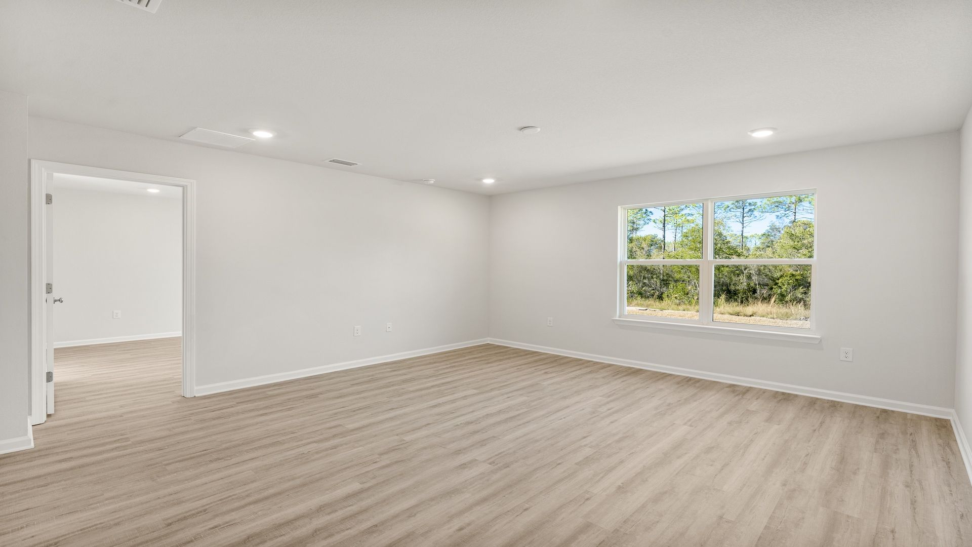 Open living room with EVP flooring and to windows next to primary bedroom entrance.