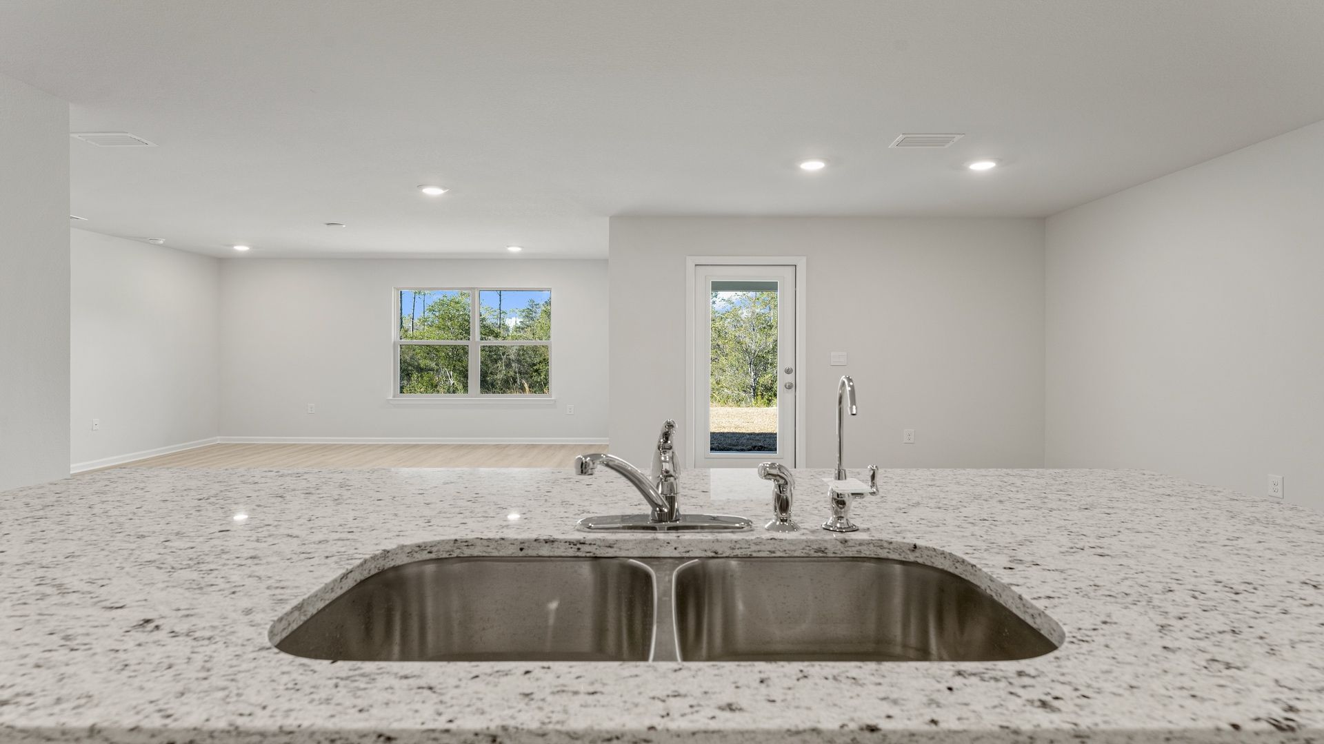 Kitchen island with undermount sink looking into dining area and back door and open living room.