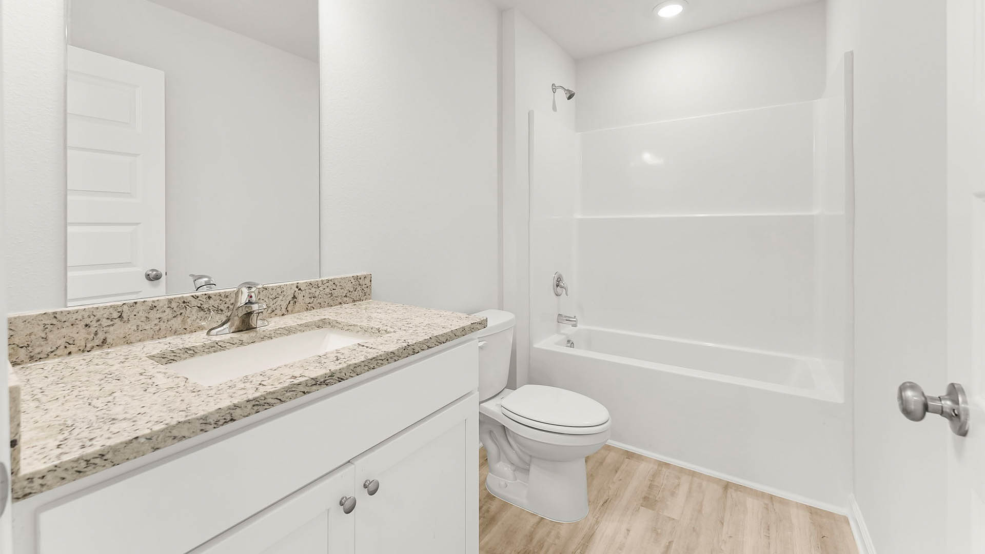 Bathroom with granite countertops and white cabinets and EVP flooring with tub and shower and toilet.
