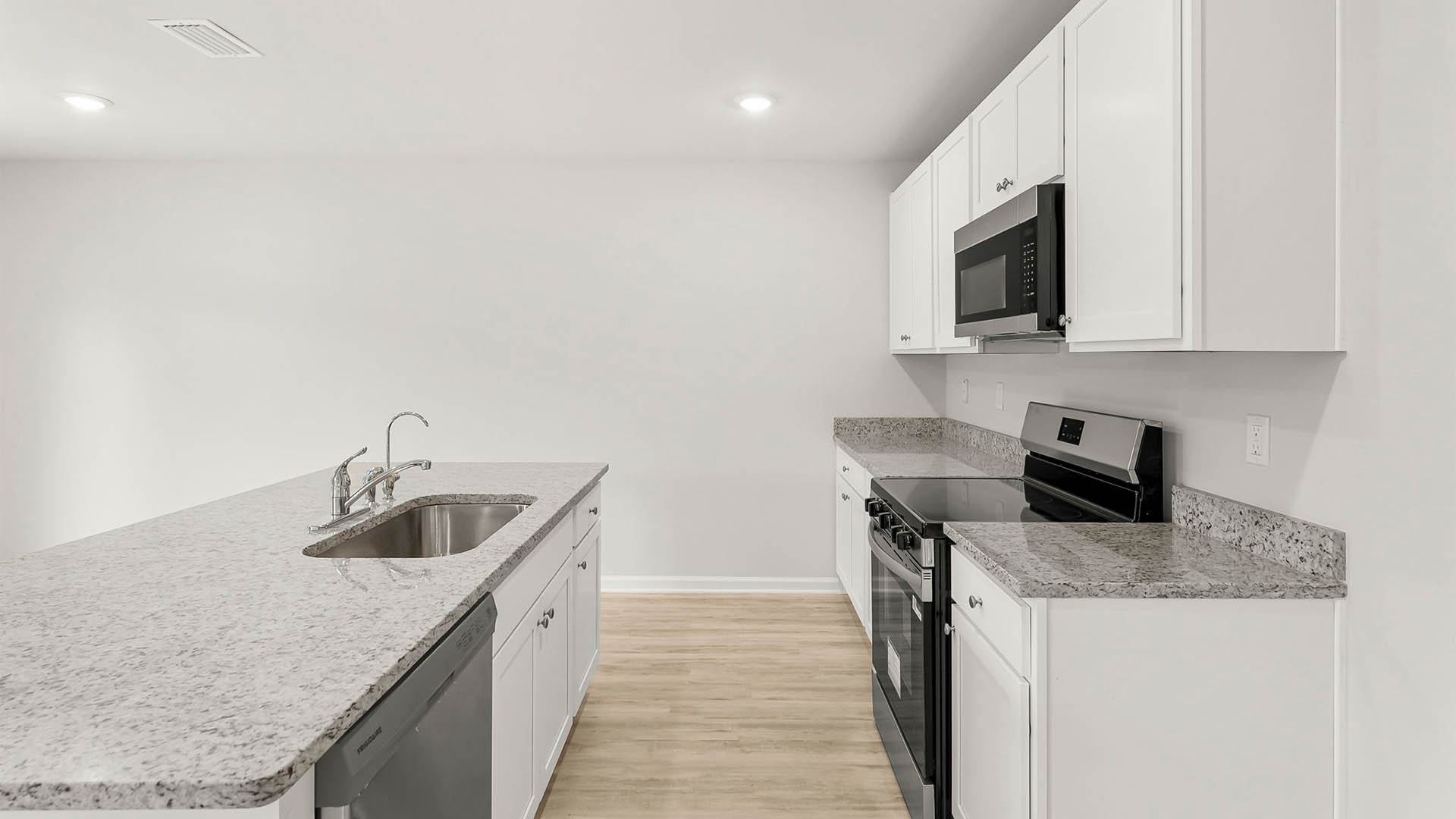 Kitchen with island and granite countertops and stainless-steel appliances and white cabinetry.