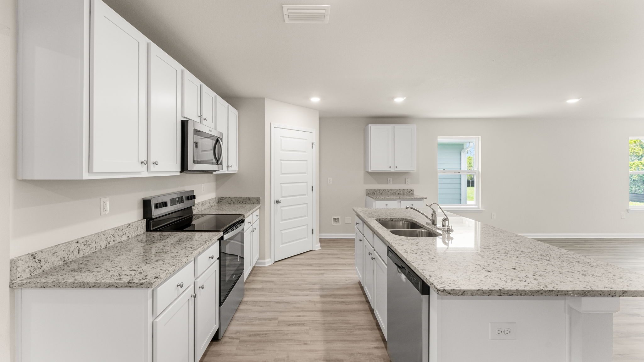 Open kitchen with island and granite countertops and stainless-steel appliances and white cabinets and pantry.
