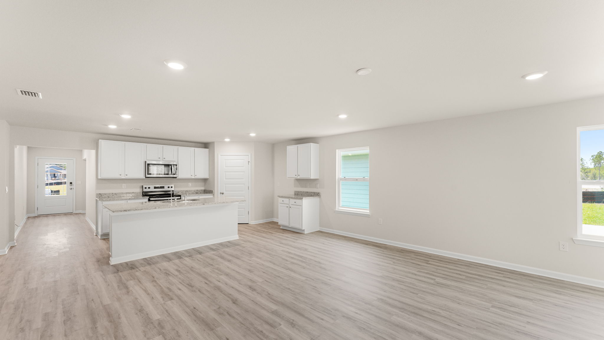 Open living room with EVP flooring and two windows and kitchen.