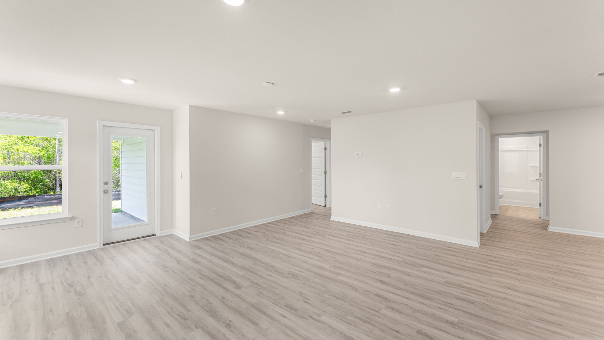 Open living room with EVP flooring and back door and bedroom entrances.