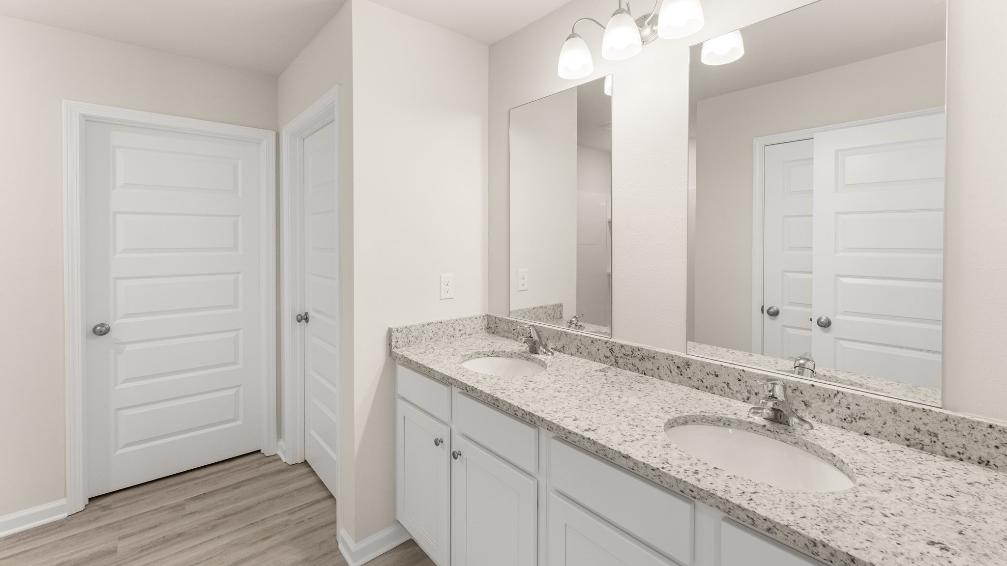 Primary bathroom with double vanity granite countertops and white cabinets.
