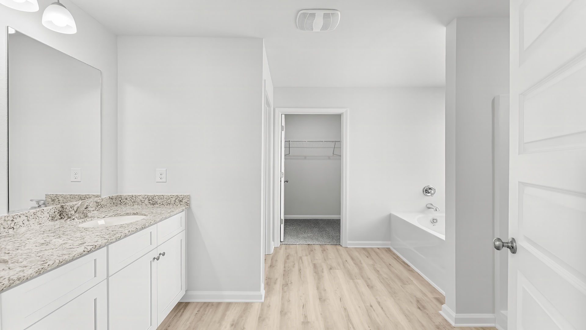 Primary bathroom with double vanity granite countertops and closet entrance.