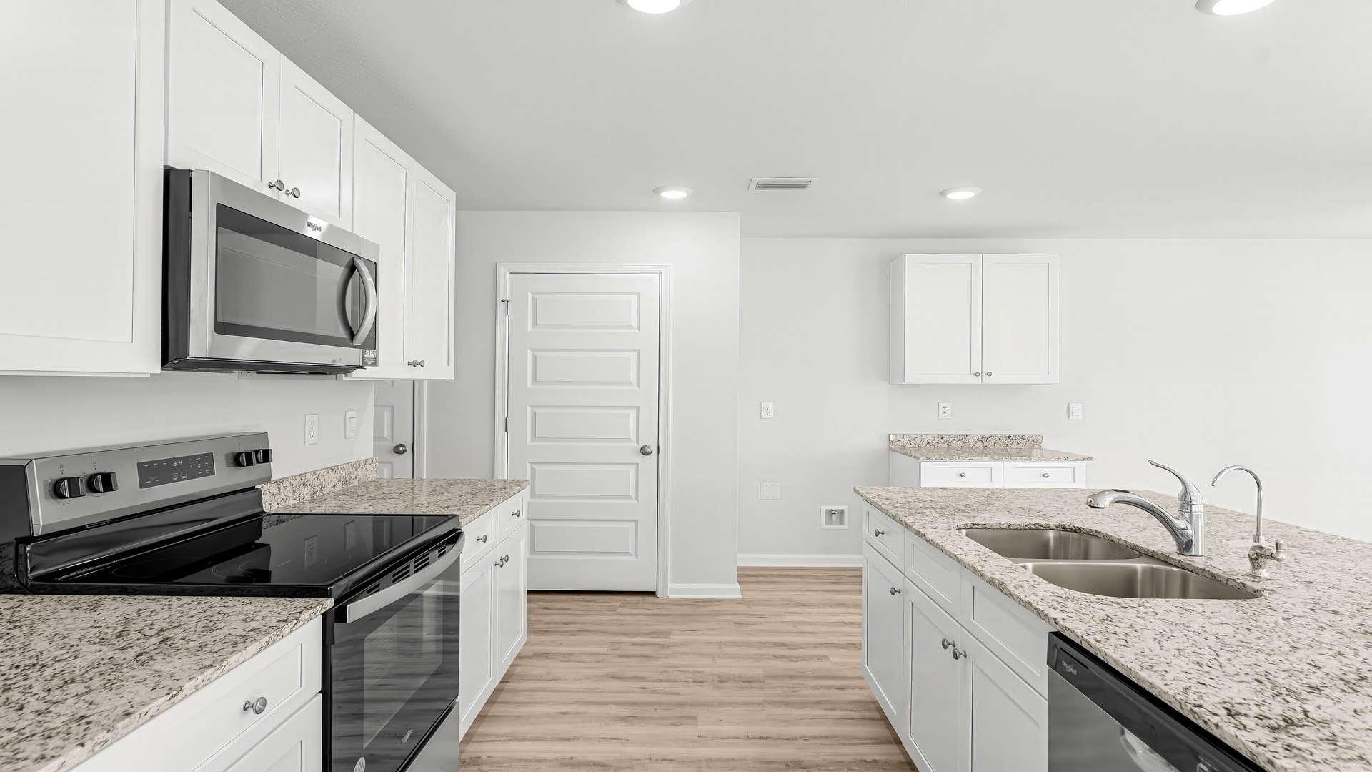 Kitchen with island and granite countertops and white cabinetry and stainless-steel appliances.
