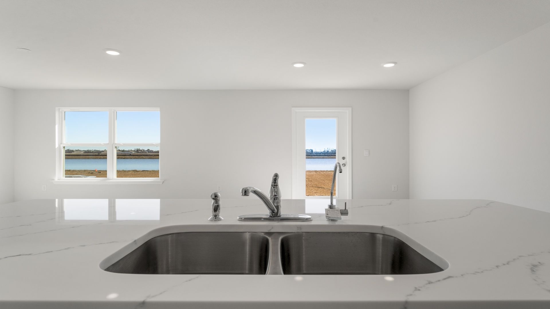 Kitchen island with quartz countertops undermount sink and back door and windows.