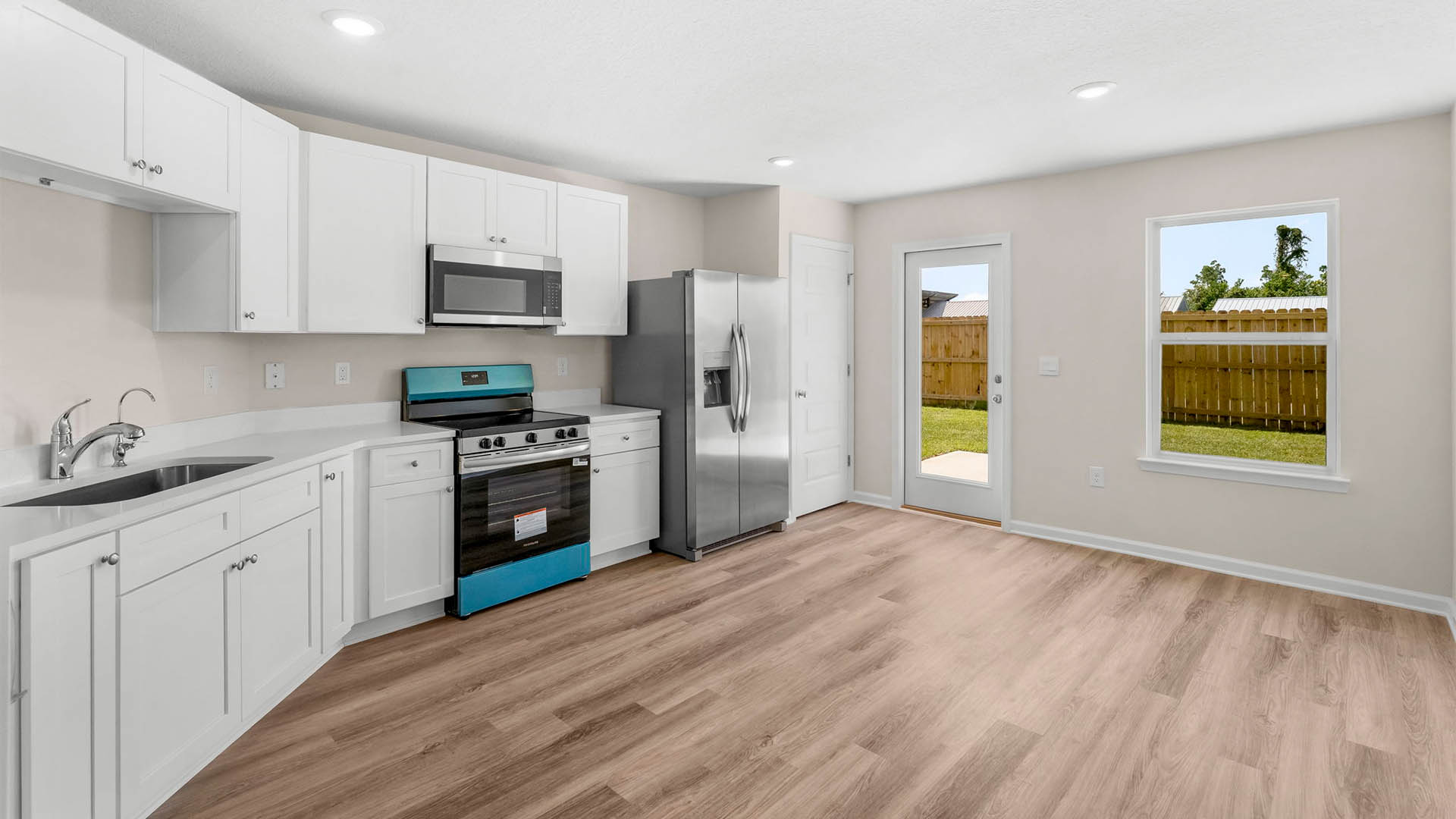 Kitchen with quartz countertops and white cabinets with stainless steel appliances and back door and dining area.