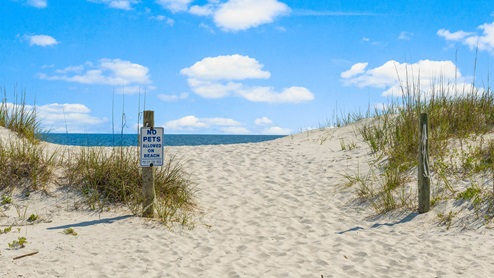 Beach entrance with sign and sand leading to water.