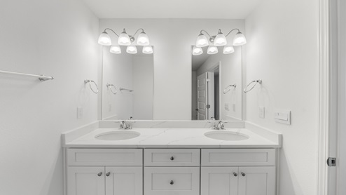 Bathroom with double vanity and quartz countertops and white cabinets.