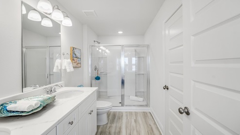 Primary bathroom with white quartz countertops and shower with glass door and toilet.