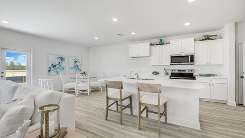 Furnished kitchen and dining room with white cabinets and quartz countertops and island.